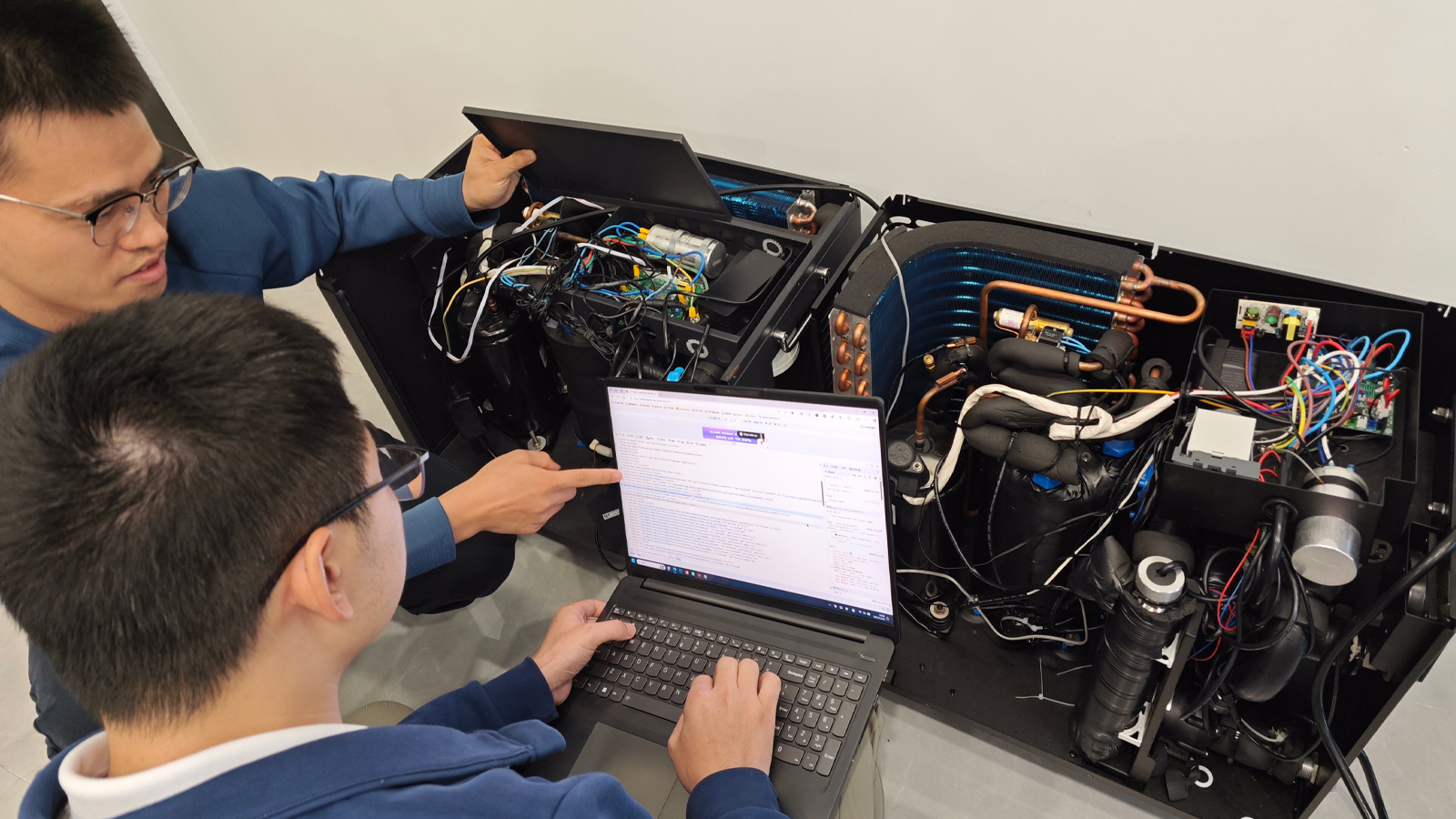 Technicians reviewing a laptop beside two open chiller units